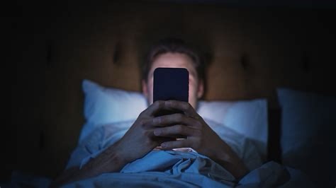 Person scrolling on phone in bed at night, symbolizing digital addiction and distraction culture in modern America