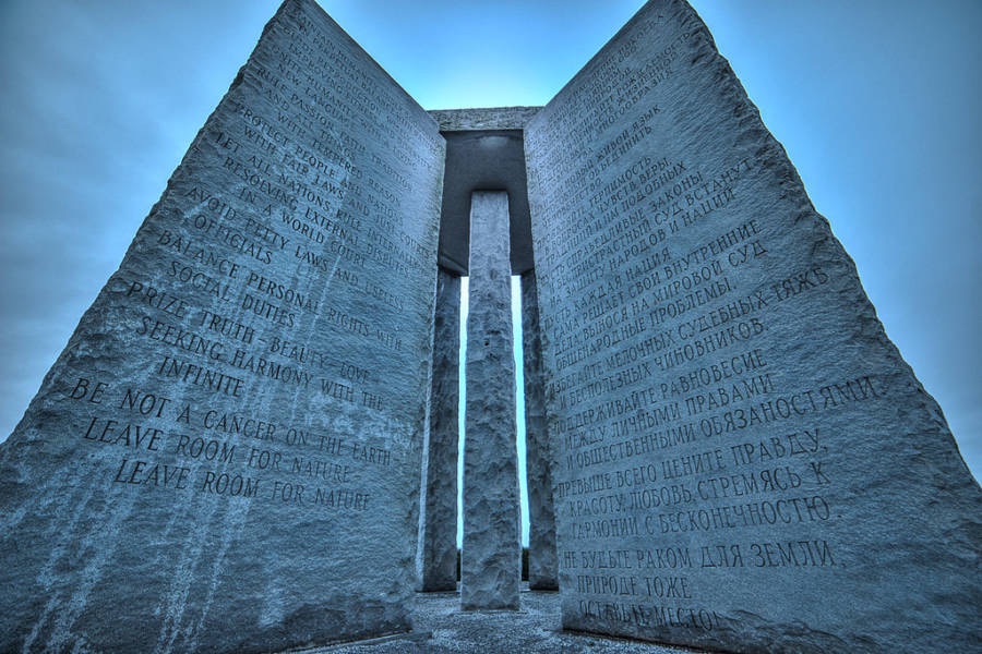 Close-up view of the Georgia Guidestones monument from below, showing engraved inscriptions in multiple languages including English and Russian, against a moody blue sky—highlighting the site’s mysterious origins and controversial messages.