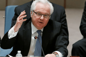 Vitaly Churkin in a suit and tie, speaking at a UN Security Council meeting with microphone in front, hand raised mid-gesture.